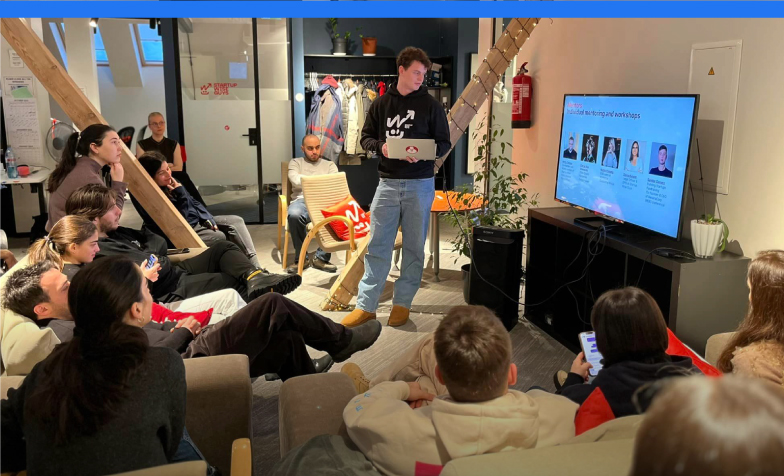 A person standing in front of a group of people sitting on couches

Description automatically generated